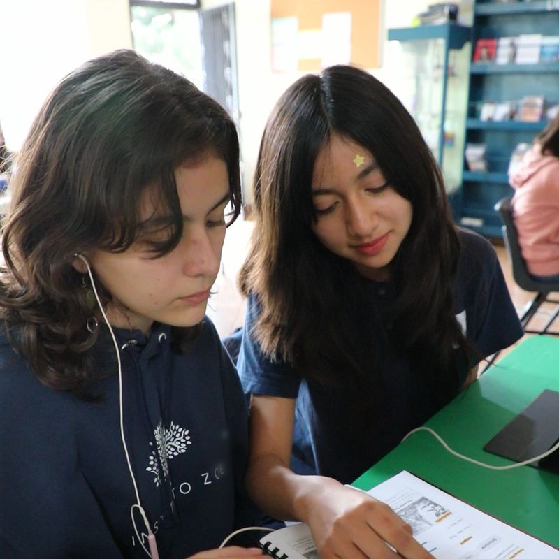 Dos alumnas de secundaria del Instituto Zoe leen juntas su cuaderno de inglés en su mesa