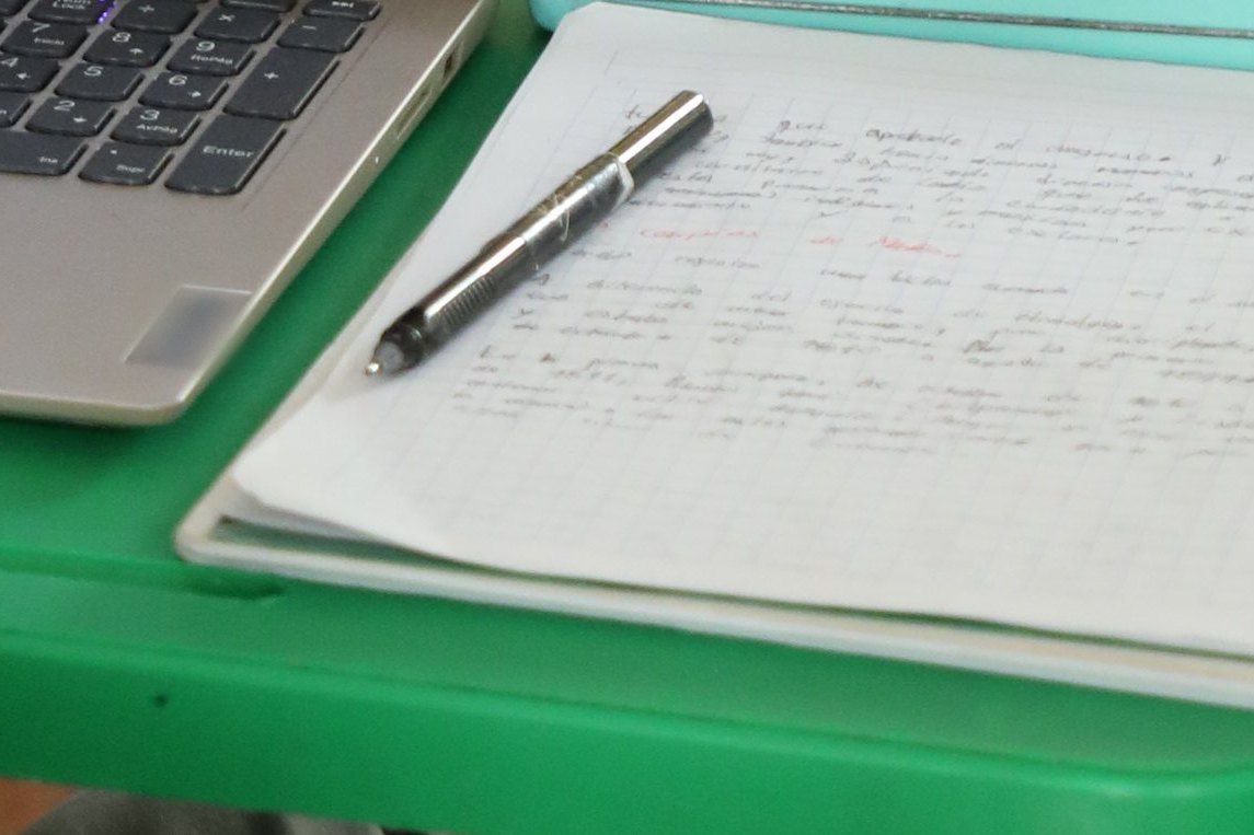 Cuaderno de apuntes y pluma junto a la laptop de un alumno de secundaria del Instituto Zoe