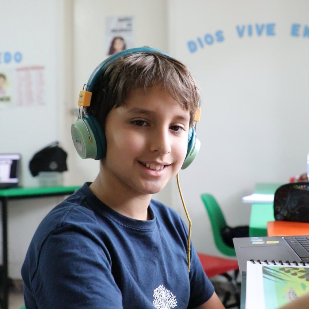 Un alumno de primaria del Instituto Zoe sonríe en su salón, bajo el letrero «Dios vive en mí»