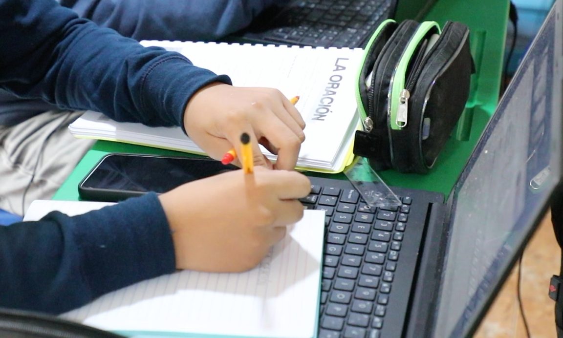 Un alumno de secundaria del Instituto Zoe escribe junto a su cuaderno «La oración» y su laptop