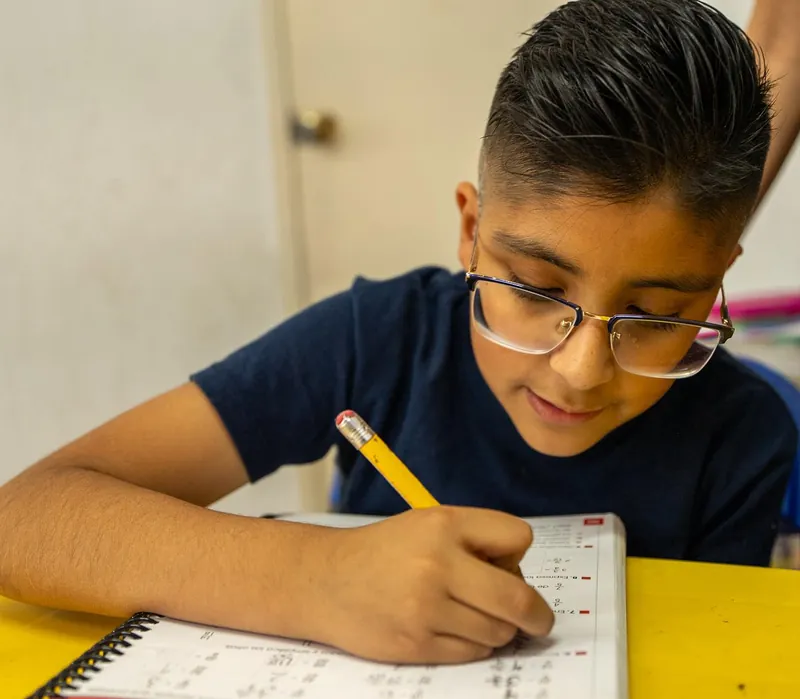 Alumno con lentes escribe en su cuaderno