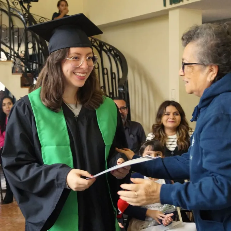 Graduada con toga y estola verde recibe su documento